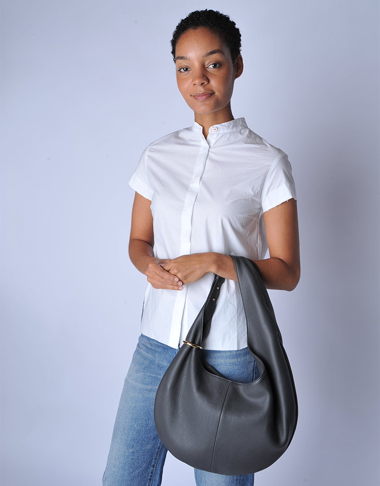Woman holding a TSATSAS HALO bag, half-moon silhouette in graphite grey calfskin leather against a plain background